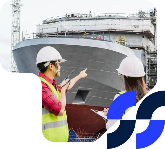 Two marine engineers wearing hard hats and high-visibility vests discuss and inspect the progress of a ship under construction.