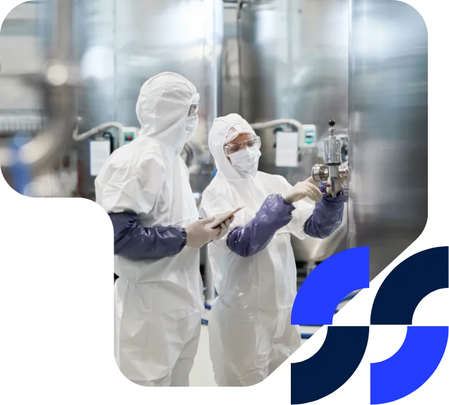 Two pharmaceutical technicians in cleanroom suits work on industrial laboratory equipment, ensuring precise measurements and safety compliance.