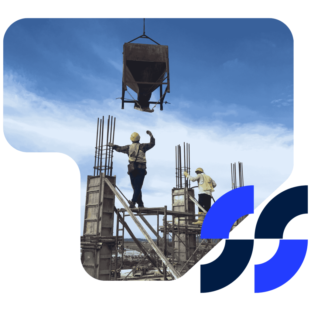 Two construction workers manage the placement of a cement pour from a suspended hopper on a building site.