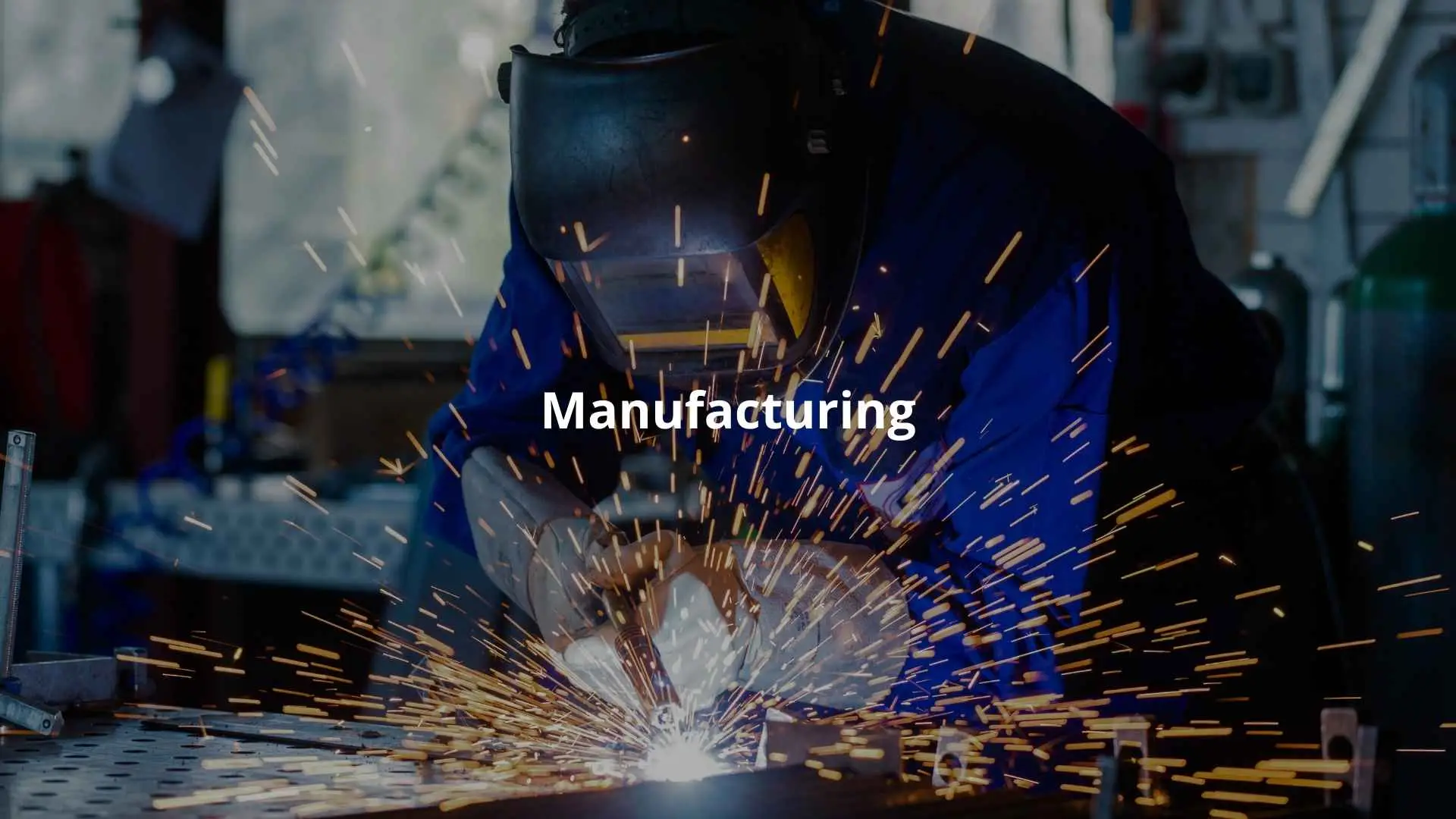 A welder in protective gear creates sparks while welding metal in a manufacturing facility.