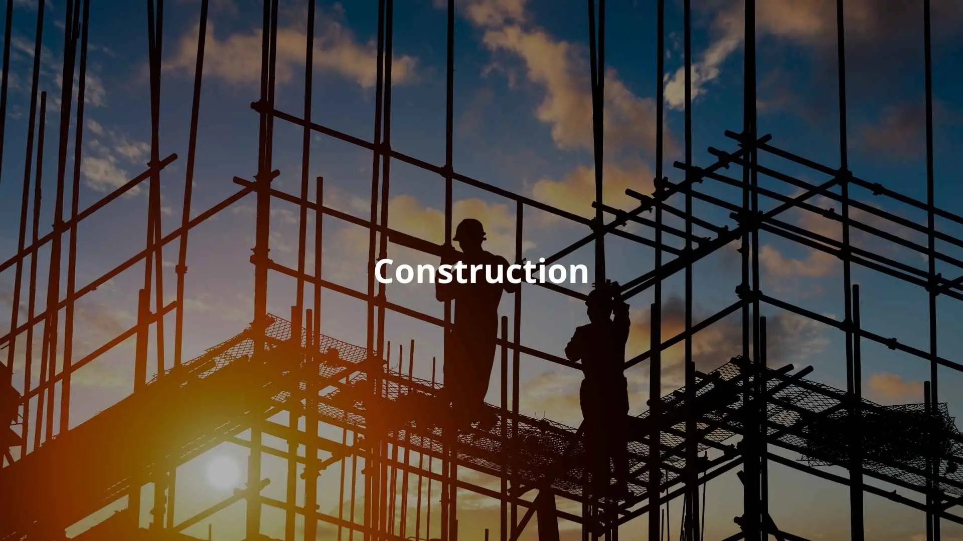 Silhouetted construction workers stand on scaffolding during sunset at a building site.