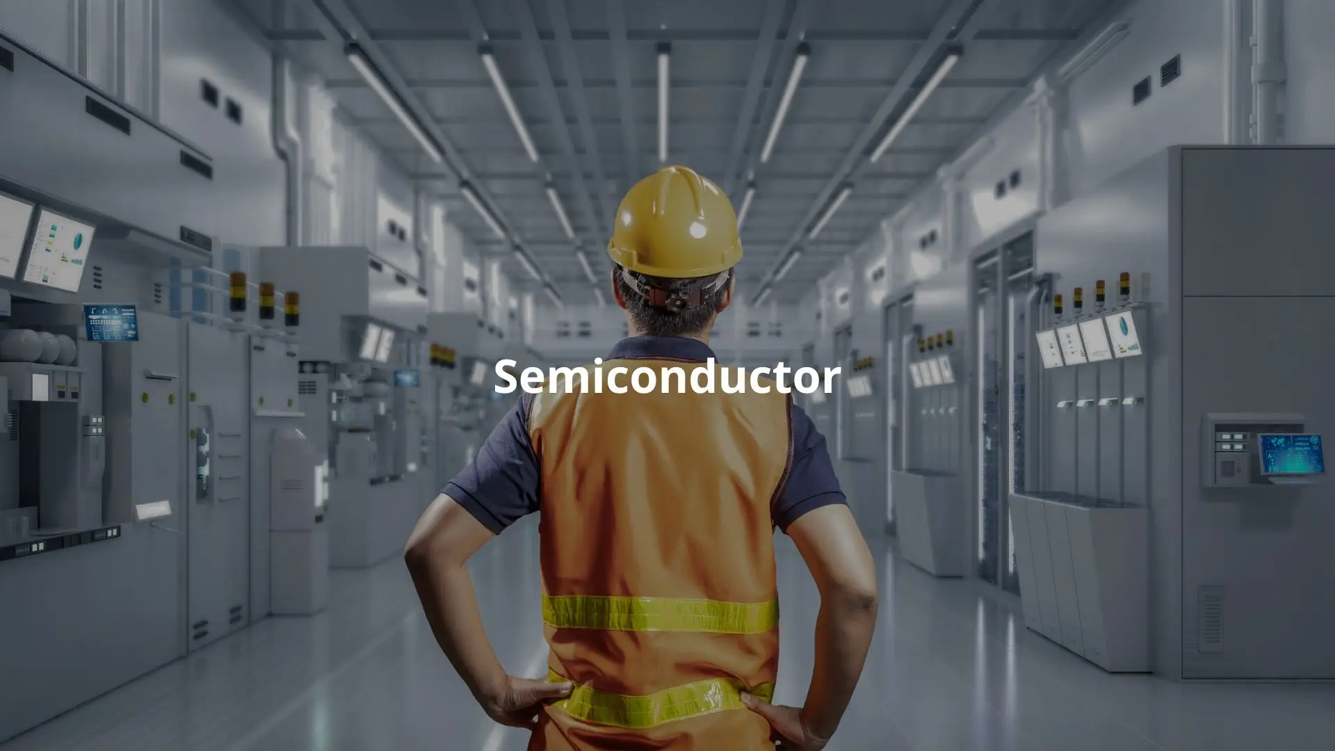 A worker in a hard hat oversees operations in a high-tech semiconductor manufacturing facility.