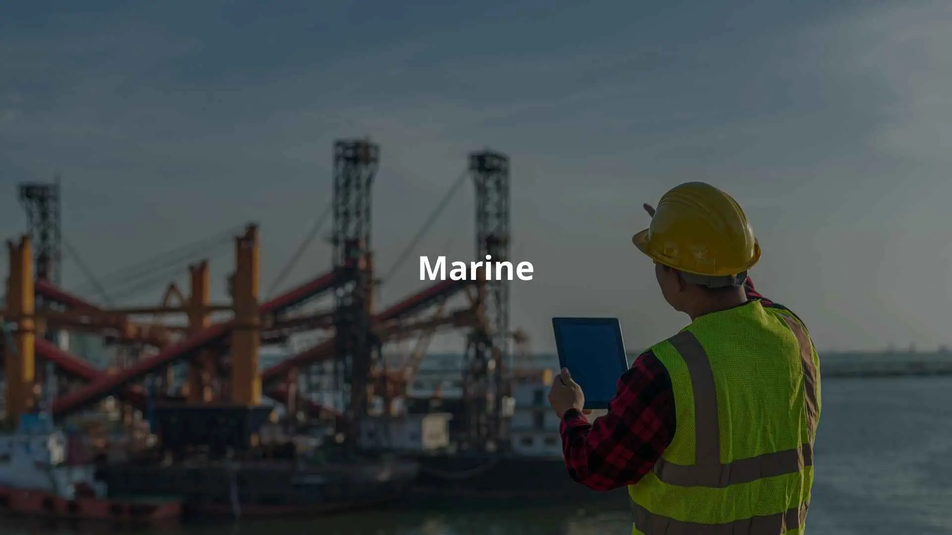 A worker in safety gear points towards a marine site, using a tablet for data review.