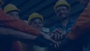 Workers in safety helmets joining hands to emphasize teamwork and workplace unity.