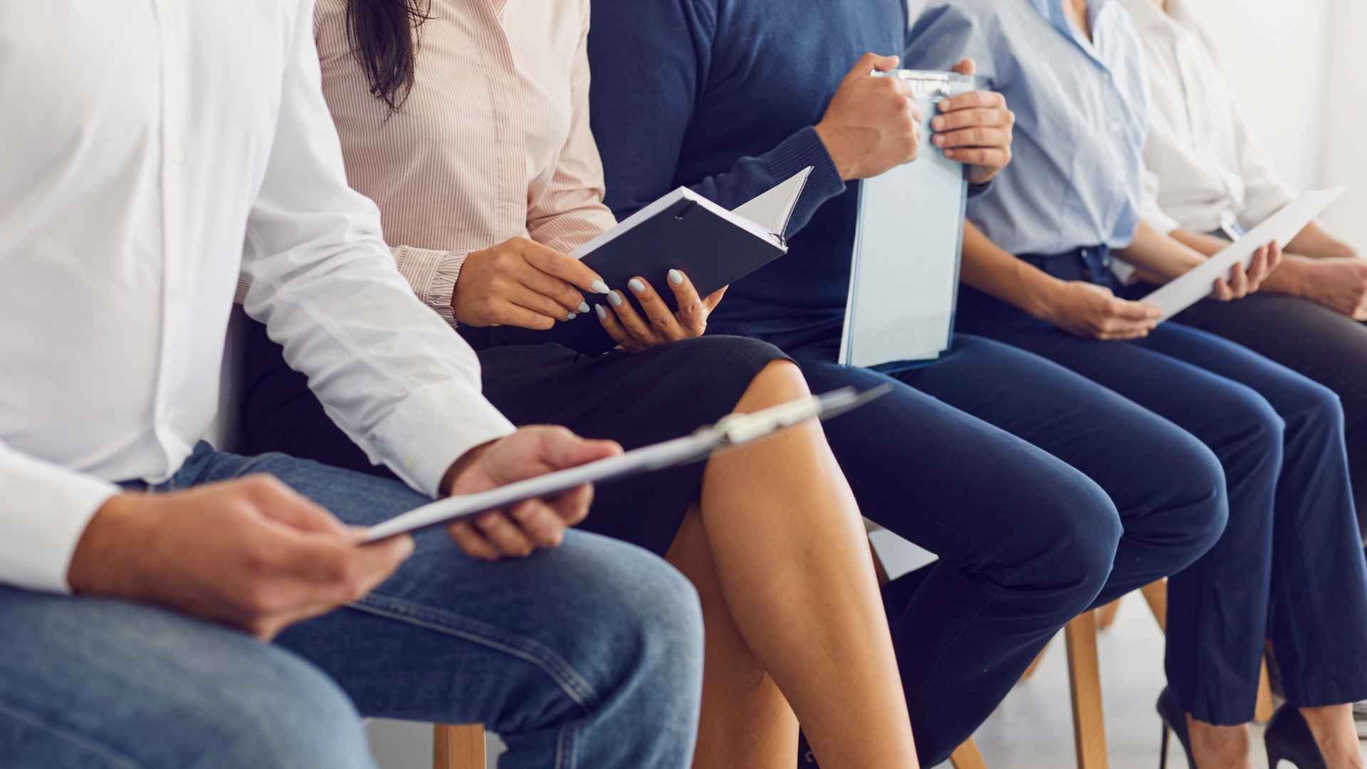 A row of job applicants sitting with documents and notebooks, preparing for an interview session.