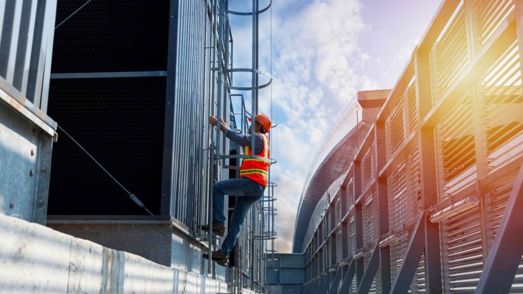 An engineer in safety gear climbing a ladder to inspect an industrial cooling system.