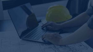 An engineer uses a laptop to check building plans, with a safety helmet resting on the desk.